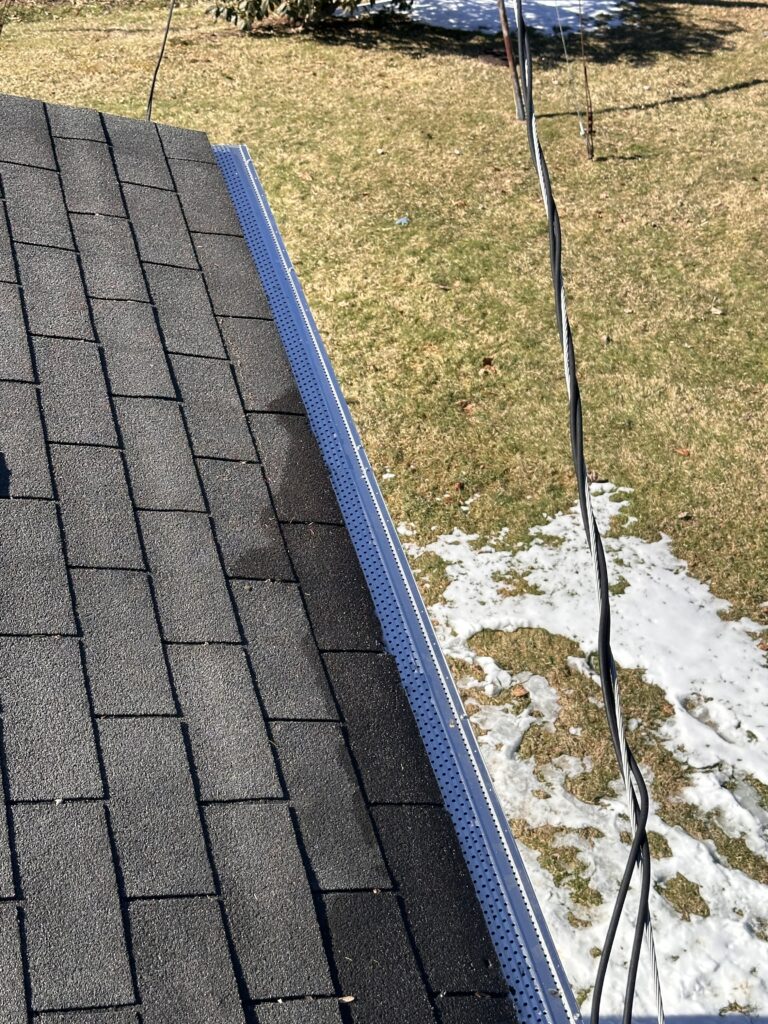 Flat Roof With Black Shingles And New Gutter Installation Visible Along The Edge With Electrical Cable Nearby