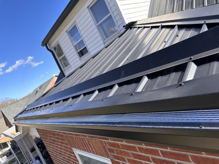 Flag Gutter Services Performing Gutter Installation On A House With A Black Metal Roof And Brick Siding